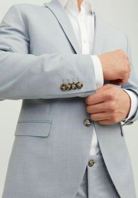 Hellblau maßgeschneiderte Sakkojacke aus strukturiertem Stoff; mit Metallknöpfen an den Ärmeln und vorne, unter einem weißen Hemd getragen.