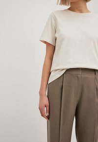 Beżowa bawełniana koszulka z krótkim rękawem, zestawiona z brązowymi spodniami o wysokim stanie, o dopasowanej strukturze i gładkiej fakturze, z bocznymi kieszeniami.