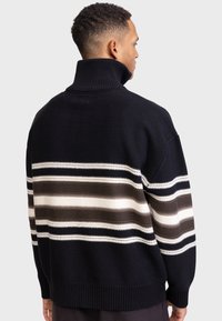 Pulover negru din tricot cu guler înalt, având dungi orizontale în nuanțe de maro, taupe și crem. Manșete și tiv ribbate, croială lejeră.