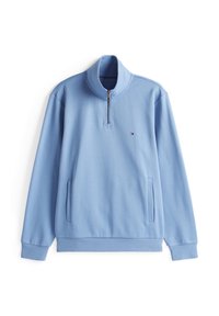 Pull-over bleu clair à demi-zip en tissu doux. Il présente un col montant, des manches longues, deux poches latérales et un petit logo sur la poitrine.