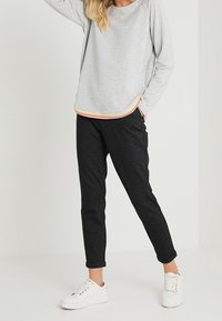Top de manga larga gris claro con dobladillo redondeado y detalles de rayas multicolores, combinado con pantalones negros entallados y zapatillas blancas.