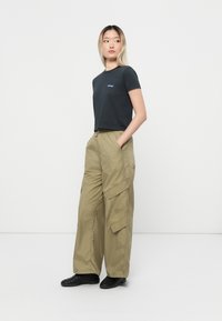 Black cropped t-shirt with a blue logo, paired with beige cargo pants featuring pockets and a relaxed fit, worn with black sneakers.