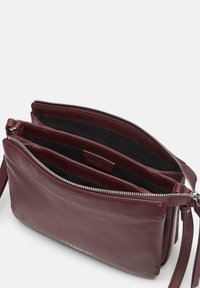 Bordowa skórzana saszetka na nadgarstek z podwójnymi przegrodami, srebrnymi zamkami błyskawicznymi i czarną materiałową podszewką.