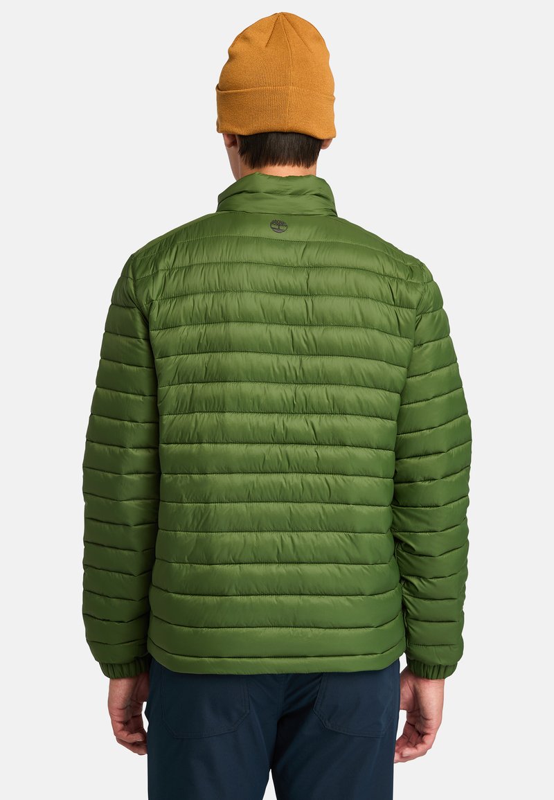 Zielona ocieplana kurtka z poziomymi przeszyciami, z kołnierzem stojącym i elastycznymi mankietami. Noszona z pomarańczową czapką beanie. Logo na górnej części pleców.