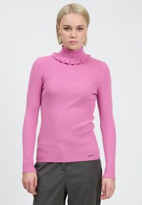 Rosa gerippter Rollkragenpullover mit Rüschensaum, tailliertem Schnitt und langen Ärmeln, kombiniert mit grauen Hosen.