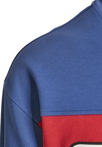 Kék és piros, rövid ujjú, kerek nyakú pulóver. Puha pamut keverék anyaga texturált részeket és kontrasztos varrási részleteket tartalmaz.