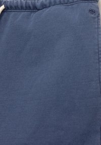 Tissu en coton bleu avec une taille élastique et un cordon blanc, montrant un petit logo brodé près du bord supérieur.