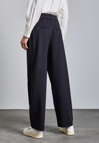 Pantaloni a gamba ampia di un blu scuro, realizzati in un tessuto morbido. Presentano due tasche posteriori e una vita sagomata, abbinati a sneaker bianche.
