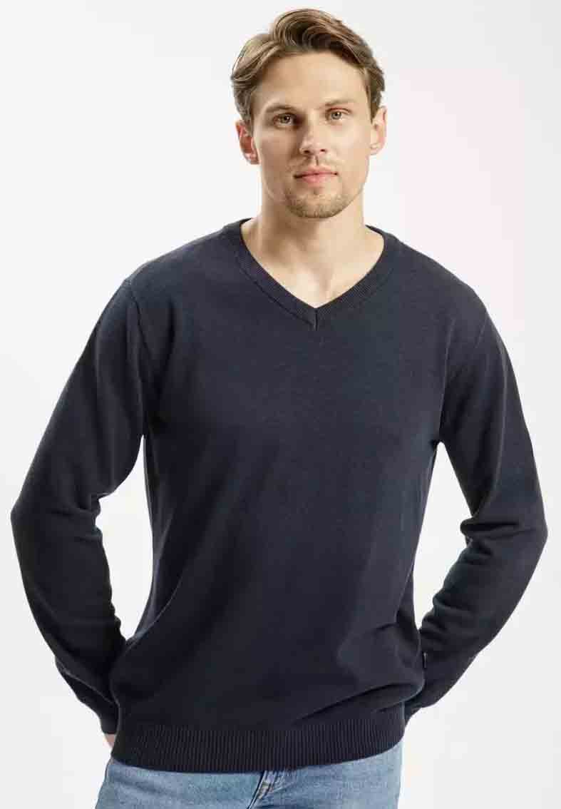 Ciemnoniebieski sweter w serek wykonany z miękkiego materiału, z długimi rękawami i ściągaczem u dołu. W zestawieniu z jasnymi dżinsami.