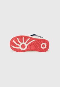 Semelle de chaussure colorée présentant un design rouge et blanc avec des rainures texturées pour une meilleure adhérence, positionnée sur un fond blanc uni.