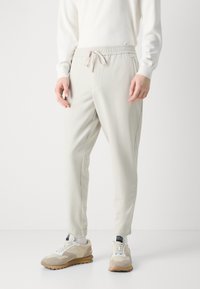 Pantalons jogger beige clair avec une taille élastique et un cordon de serrage. Dispose de poches latérales et de jambes fuselées, fabriqués à partir d'un matériau lisse et doux.
