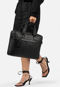 Borsa per laptop in pelle nera con doppi manici superiori, marchio impresso e forma rettangolare. Presenta un'etichetta staccabile e una texture liscia.