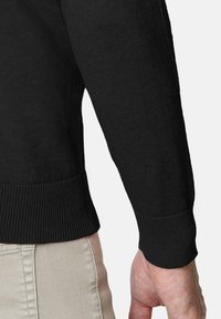 Suéter negro de punto con dobladillo y puños acanalados, mostrando un primer plano de la manga. Textura suave, corte regular y detalles de diseño minimalistas.