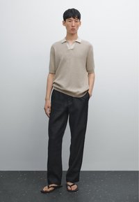Polo in maglia beige a maniche corte, abbinato a pantaloni neri larghi e ciabatte nere; texture liscia, design minimale.