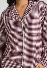 Bordeaux en witte geblokte pyjama-top met een kraag, knoopsluiting en zak. Zacht stof met contrasterende bies langs de randen.