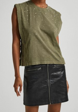 Olivgrünes ärmelloses Oberteil mit Strassverzierungen, kombiniert mit einem schwarzen Minirock aus Leder mit Reißverschlusstaschen und Frontverschluss.