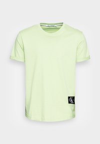 T-shirt vert clair à manches courtes et col rond avec des poignets roulés et un patch logo Calvin Klein Jeans noir près de l'ourlet inférieur.