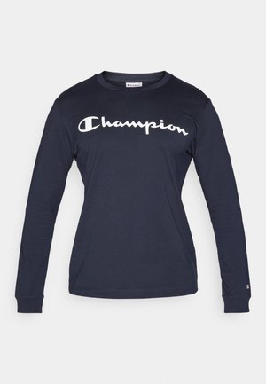 Tumesinine pikkade varrukatega puuvillane t-särk. Rinnal on silmapaistev valge "Champion" logo ning võrgutud mansetid.