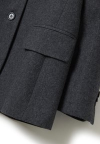 Blazer de mezcla de lana de color gris oscuro con solapas de muesca, dos botones y un bolsillo de parche con tela texturizada y una silueta entallada.