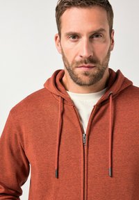 Roter Fleece-Zip-Hoodie mit texturierter Oberfläche, Kordelzügen und einem kontrastierenden Reißverschluss. Verfügt über ein weiches Innenfutter und ein schlichtes Design.