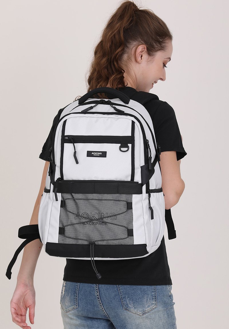 Zaino bianco e nero con vari taschini a zip, dettagli in rete, spallacci regolabili e schienale imbottito per il comfort.