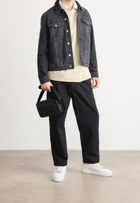 Svart denimjacka med silverknappar, beige tröja, svarta byxor, vita sneakers och en liten svart handväska. Släta material, avslappnad design.