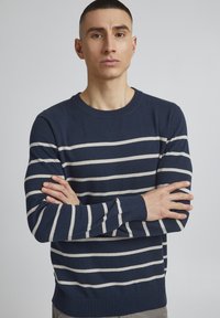 Marineblå stripete genser med lysegrå horisontale striper, strikket tekstur, rund hals og tettsittende mansjetter, vist mot en ensfarget bakgrunn.