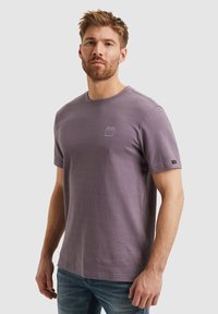 Camiseta morada texturizada de manga corta y cuello redondo, que presenta un pequeño logo en el pecho y un diseño limpio y sencillo.