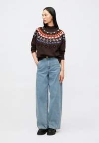 Maglione marrone a maglia con motivi geometrici colorati, abbinato a jeans a gamba larga color azzurro chiaro a vita alta e scarpe nere spesse.