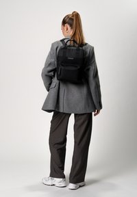 Zaino nero con un design strutturato, dotato di manico superiore, spallacci regolabili e tasca frontale con zip. Tessuto testurizzato e dettaglio del logo.