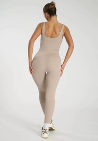 Ljusbeige bodysuit med scoop back, figurnära design och minimala sömnadsdetaljer, tillsammans med mönstrade sneakers och vita strumpor.