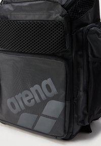 Zaino nero con tasca in rete strutturata, più scomparti con cerniera e un grande logo Arena grigio sul davanti. Realizzato in tessuto resistente.