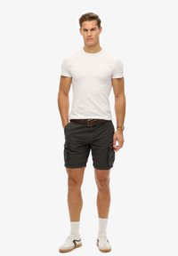 Grijze cargoshorts met zijzakken, witte nauwsluitende t-shirt, bruine riem, opgerolde witte sokken en casual witte sneakers met zwarte accenten.