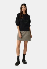 Felpa nera con vestibilità rilassata e logo testurizzato, abbinata a una gonna a quadri corta. Il modello indossa stivali neri chunky.