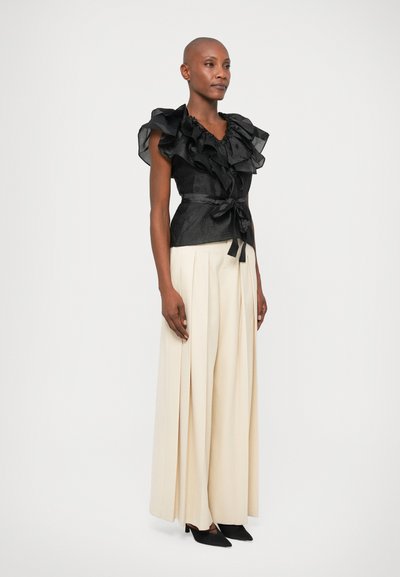 Must mustrihiga ülaosa tekstureeritud kangaga, vööga taljes, koos beeži laia jalgadega pükste ja mustade kontsakingadega. Tavaline taust.