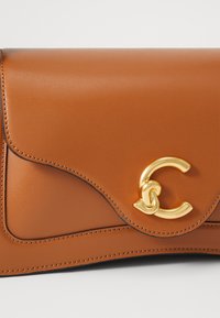 Brown leather clutch bag with a curved flap, featuring a gold circular clasp and contrasting stitching along the edges.