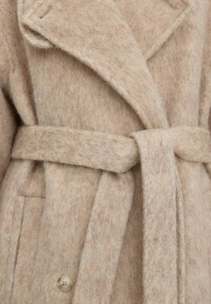 Béžový vlněný kabát se širokými klopami, zavazovacím pásem v pase a viditelným knoflíkem blízko spodní části na přední straně.