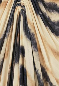 Tyg med en tie-dye-mönster som har beige, bruna och mörkblå nyanser; strukturerad med samlade sektioner som skapar en draperad effekt.