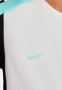 Top sportivo Nike con un corpo bianco a trama, maniche nere e un logo acquamarina sul petto. Il colletto ha un design classico a girocollo.