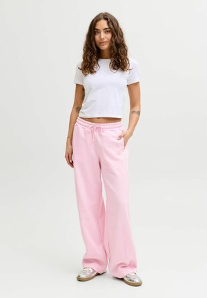 Light pink cotton sweatpants with a relaxed fit, drawstring waist, and side pockets, paired with a white cropped t-shirt. Silver sneakers.