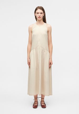 Μπεζ μάξι φόρεμα από βαμβάκι με εφαρμοστή μπούστο και αέρινη φούστα, με λεπτές τιράντες και σούρα στη μέση. Συνδυάζεται με καφέ δερμάτινα παπούτσια με κορδόνια.