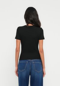 Μαύρο κοντομάνικο μπλουζάκι με εφαρμοστή σχεδίαση και ριμπ ύφασμα, συνδυασμένο με μπλε τζιν ψηλόμεσο με πίσω τσέπες.