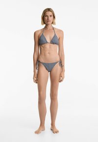 Bikini v námořnické modré a bílé barvě s vzorem, obsahující top s halter krkem a posuvnými trojúhelníky, a spodní část s vázacími detaily po stranách. Hladká textilie.