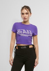 Violets krūšturis no kokvilnas ar īsām piedurknēm. Priek�šā ir balta "Von Dutch Originals" grafikā skriptveida fontā.