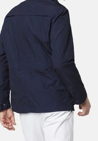 Veste légère bleu marine avec fermeture éclair, poignets à bouton et empiècement au dos. Fabriquée en tissu texturé et respirant avec une coupe décontractée.