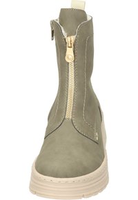 Bottines vert olive avec une fermeture éclair dorée sur le côté, des détails de couture, et une semelle de couleur claire. Texture en daim lisse avec un bout rond.