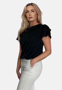 Czarna bluzka z krótkim rękawem i falbaniastymi ramionami w połączeniu z jasnymi, dopasowanymi spodniami, prezentującymi gładką fakturę i prosty design.