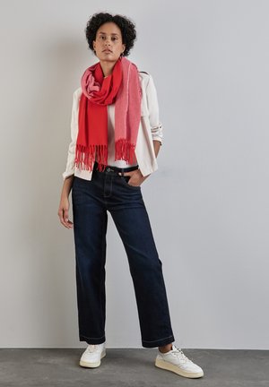 Sciarpa in misto lana rossa e rosa con frange, camicia bianca a maniche lunghe, jeans a gamba larga in denim scuro e sneakers bianche.