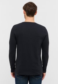 Langärmliges schwarzes Shirt mit einer strukturierten Oberfläche, rundem Ausschnitt und einem Saum, der hinten etwas länger ist.