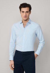 Lichtblauw, overhemd met lange mouwen en een slim fit. Heeft een puntige kraag, een voorste knoopsluiting en een klein geborduurd detail op de borst.